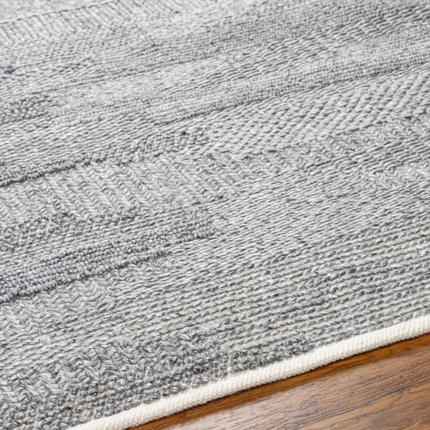 Close-up of the hand woven Chepe Area Rug. Charcoal, light gray, and dark gray recycled PET yarn create a textured pattern. Texture