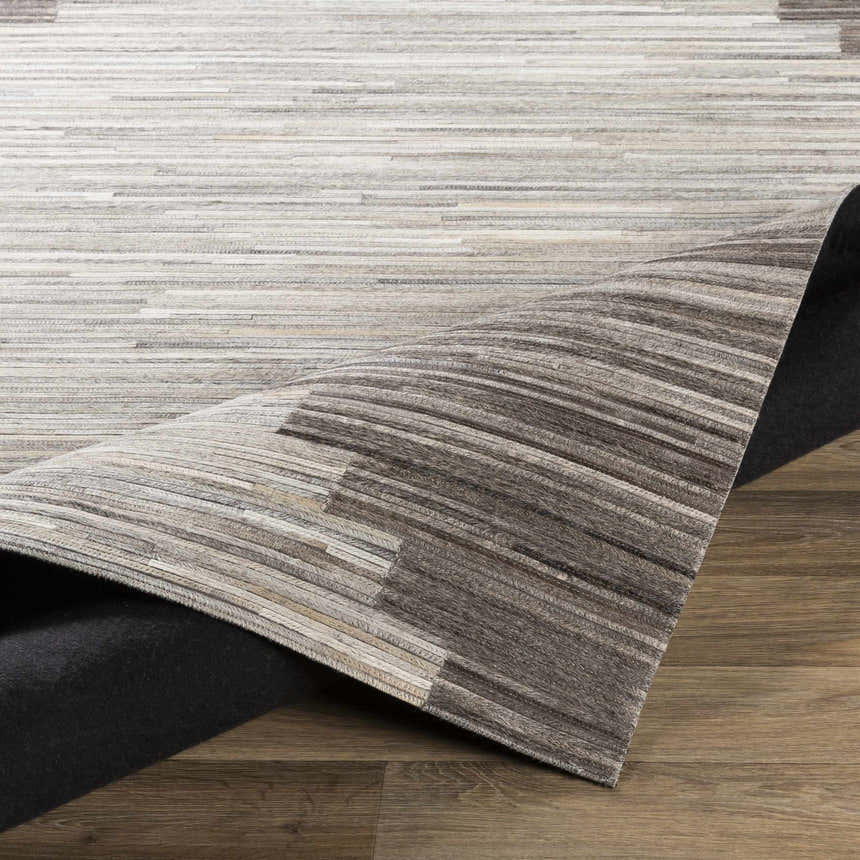 Close-up of the Shearwater Premium Rug. Hair on hide rug in beige, charcoal, and gray tones with a linear pattern. Fold