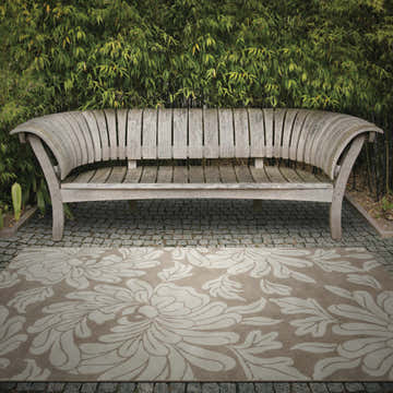Outdoor scene with a beige Sherard Area Rug featuring a floral pattern under a wooden bench. Roomscene-Rectangle