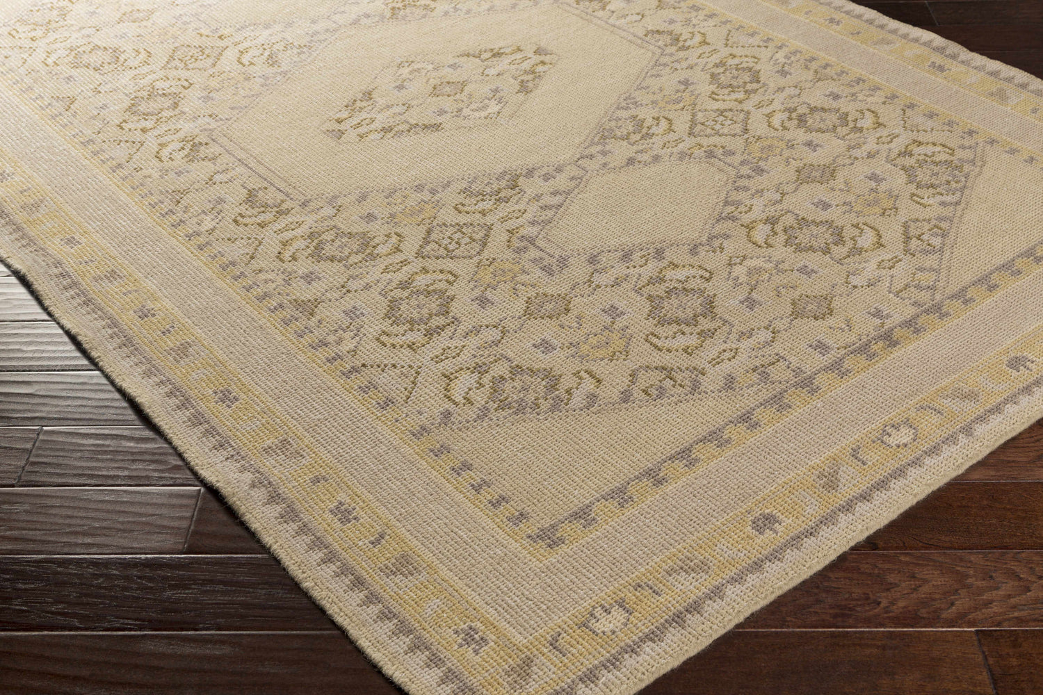 Close up of the hand knotted Shoemakersville Area Rug, beige and mustard tones, on dark wood floors. Corner
