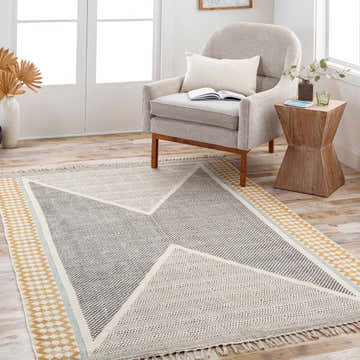 Living room scene with a Sherbrooke Area Rug in black, beige, mustard, and teal, styled under a chair and side table. Roomscene-Rectangle