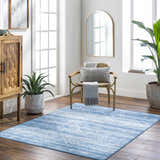 Bright, airy living room with a blue Blake Arctic Sky Washable Area Rug, wood floors, and a woven chair. Roomscene-Rectangle