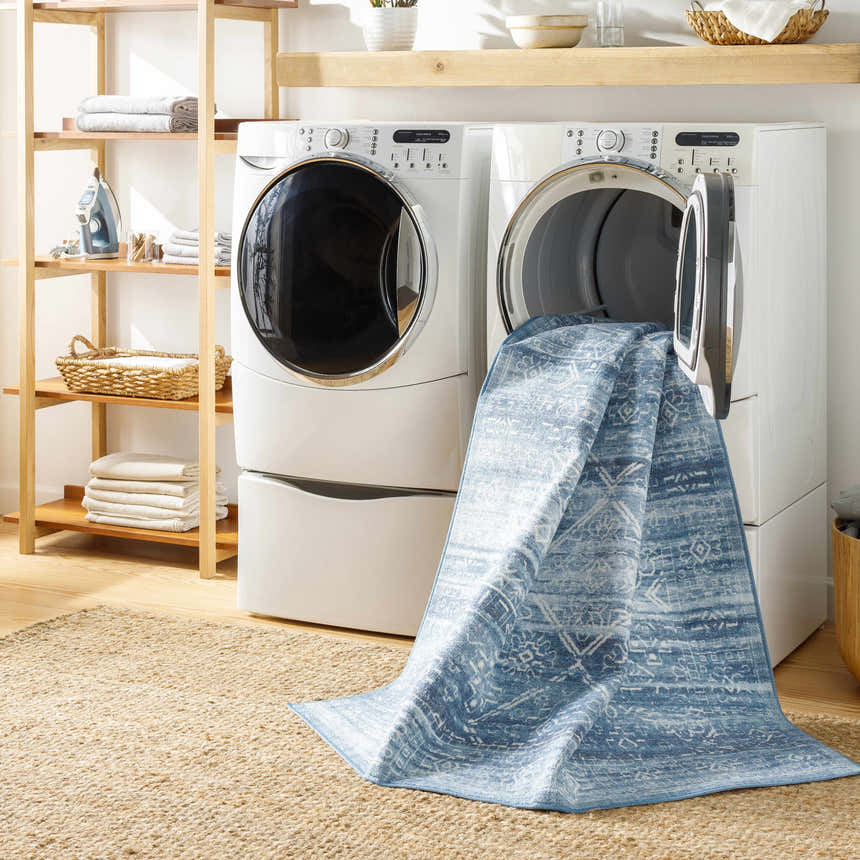 Laundry room scene with a Blake Arctic Sky Washable Area Rug partially pulled from a front load washer. Jute rug on the floor. Washing-Machine