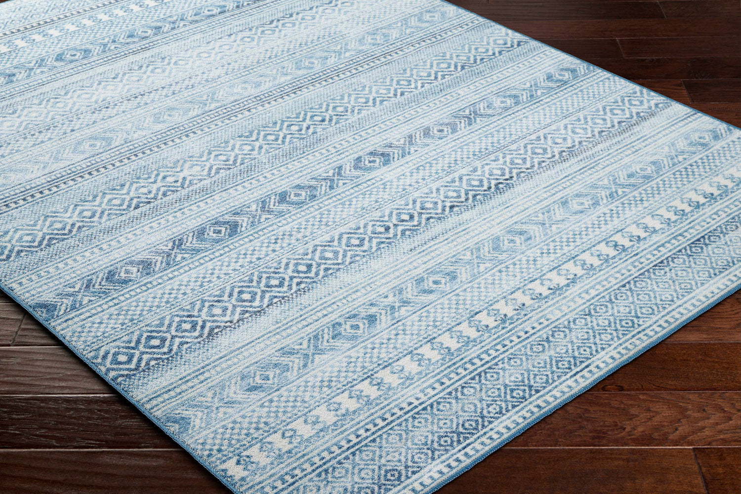 Close-up of the Gizeh Arctic Stone Washable Area Rug featuring a blue and white geometric pattern on a dark wood floor. Corner