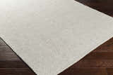 Close-up of the hand woven Shorterville Area Rug. Cream, light gray, and light slate natural fiber rug on dark wood floor. Corner
