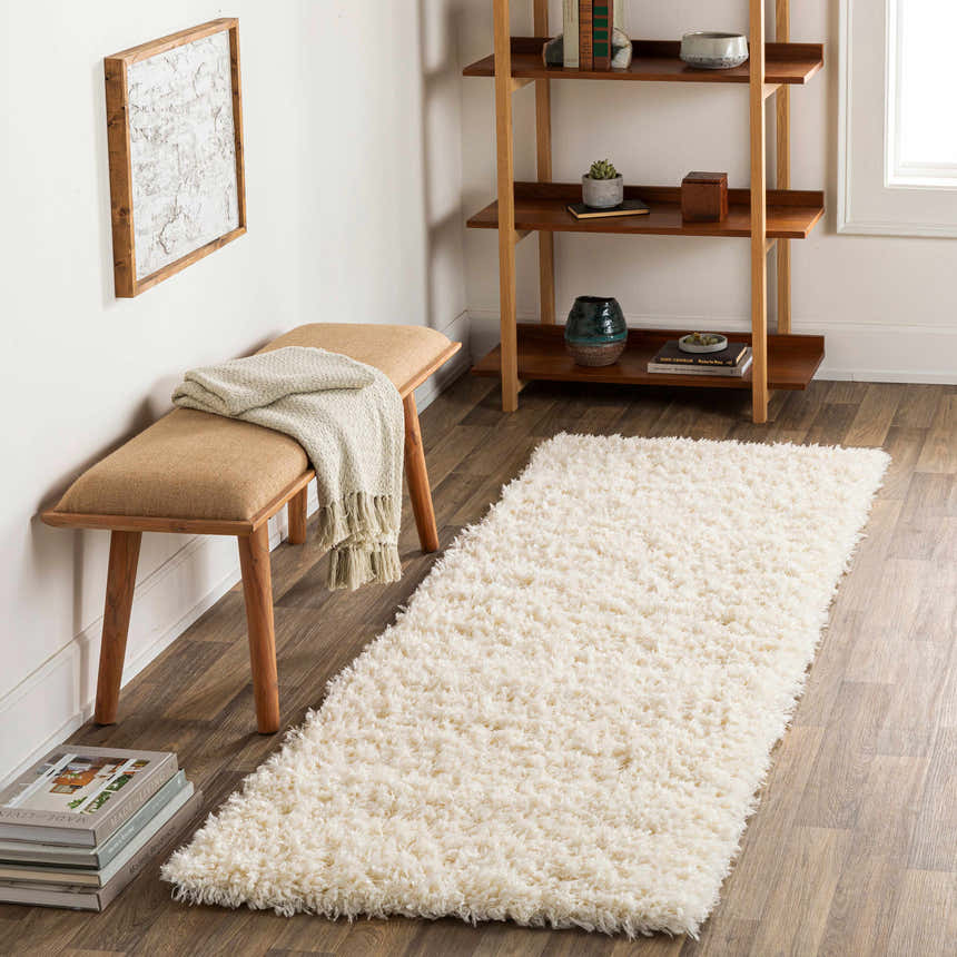 Living room scene with a cream Siari Solid Plush Rug, wooden bench, and bookshelf. Roomscene-Runner