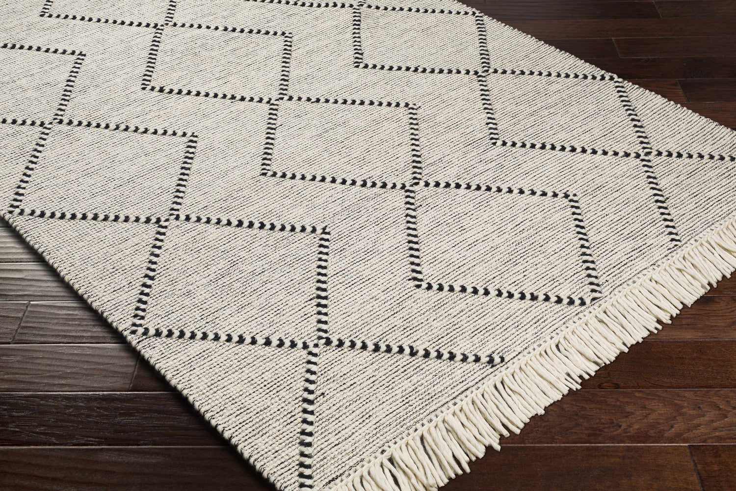 Close-up of the Siguinon Area Rug. Cream wool rug with black geometric diamond pattern and fringe. Hand woven. Corner