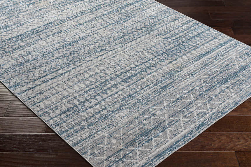 Close-up of the Tambac Blue Washable Area Rug featuring a distressed geometric pattern in shades of blue and gray. Corner