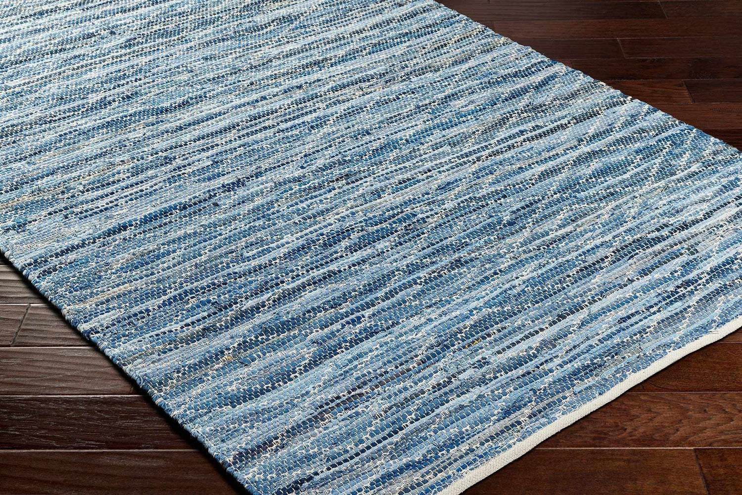 Close-up of the hand woven Gurit Blue Area Rug. Features stripes of arctic sky, harbor blue, and light gray recycled fabric. Corner