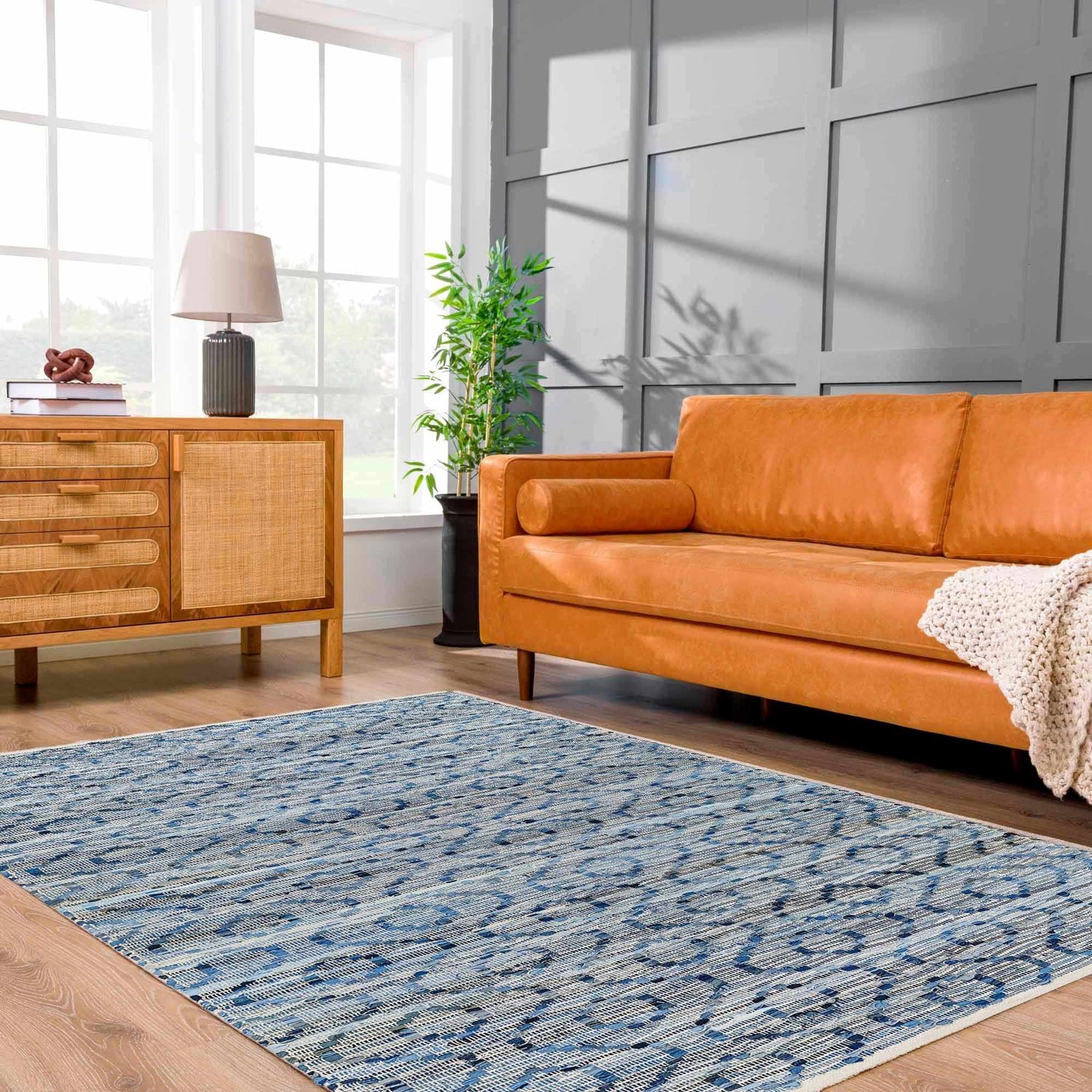 Living room scene with a Gurit Blue & Brown Area Rug, tan leather sofa, wood cabinet, and gray accent wall. Roomscene-Rectangle