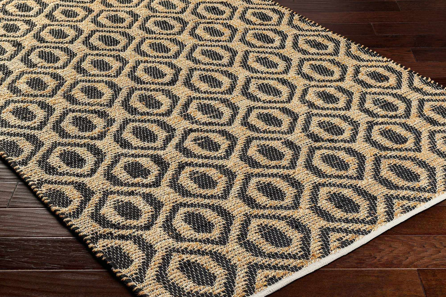 Close-up of the Isaye Charcoal Area Rug showing its jute texture and geometric dark beige and black pattern. Corner