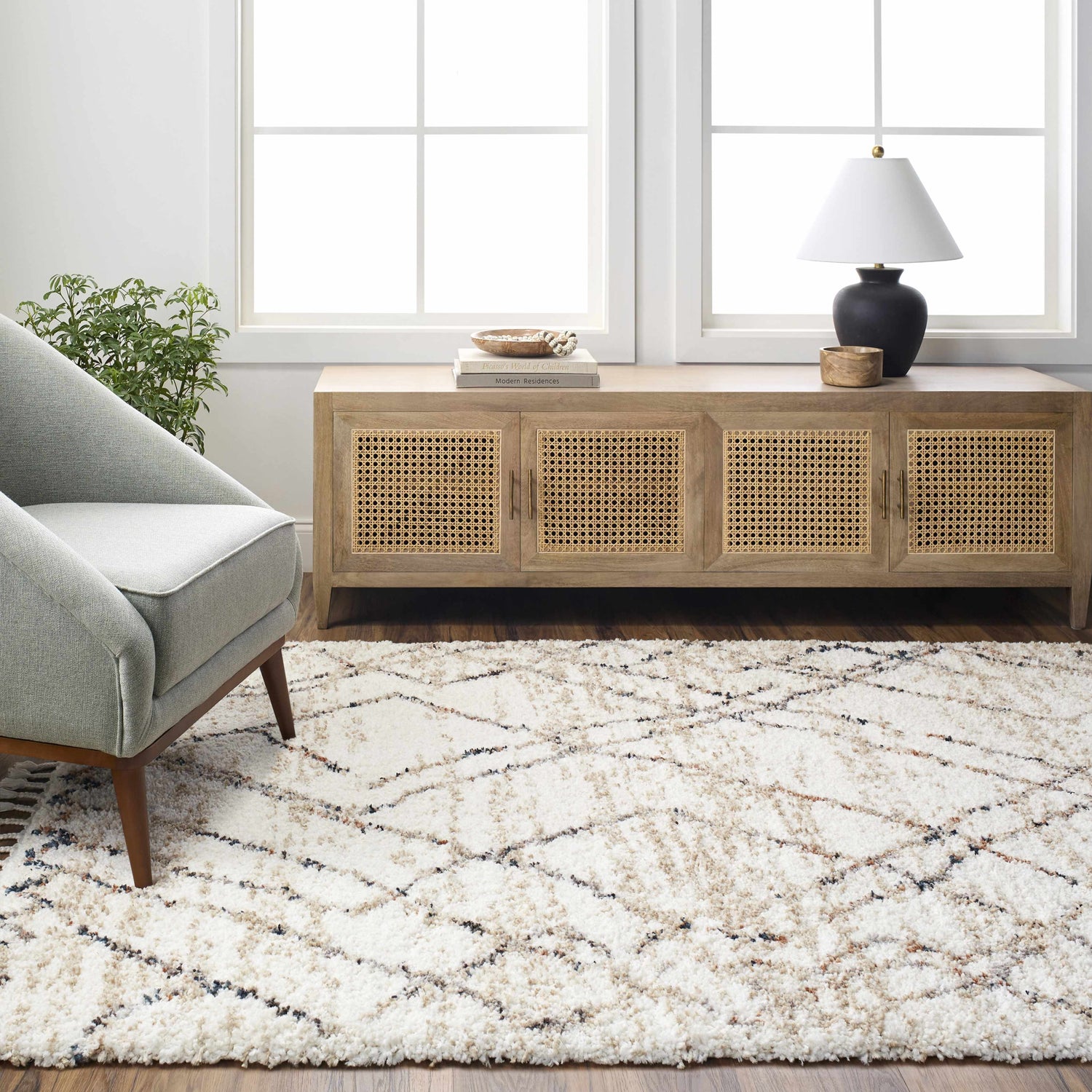 Living room scene with a Hersz Cream Area Rug, gray chair, and wood cabinet. Neutral tones and natural light. Roomscene-Rectangle
