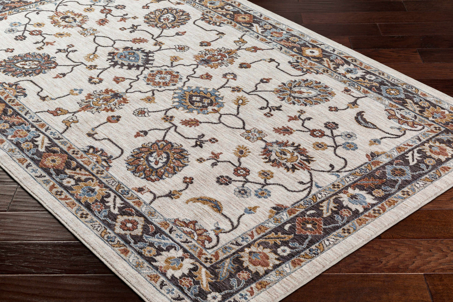 Close-up of the Adjoa Area Rug showcasing its floral pattern, neutral background, and brown, gold, and blue accents. Corner