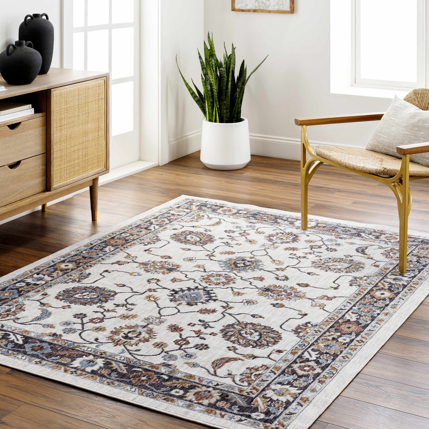 Living room scene with a light floral Adjoa Area Rug, wood floors, a cane chair, and a wood cabinet with black vases. Roomscene-Rectangle