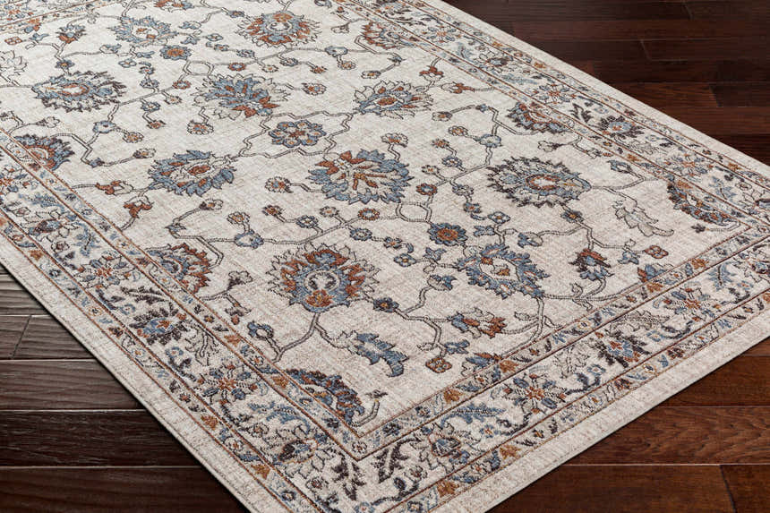 Close-up of the Ardin Cream Area Rug showing its floral pattern in blue, brown, and tan on a dark wood floor. Corner