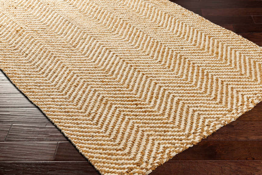 Close-up of the Aren Area Rug showing a geometric chevron pattern in natural jute and light beige colors. Corner