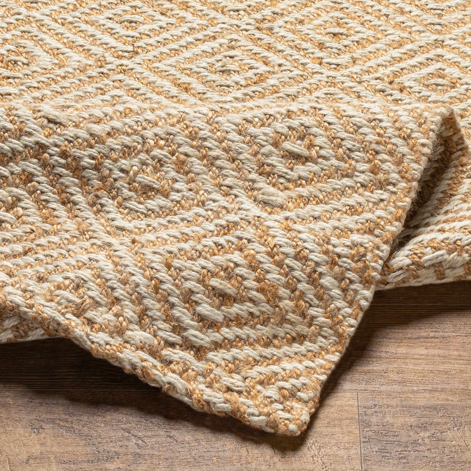 Close-up of the hand woven Eriko Area Rug showing its geometric diamond pattern and natural jute texture in tan and beige. Fold