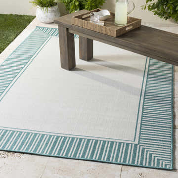 Outdoor patio scene with Skipton Area Rug in teal and white, with striped border, under a wooden bench. Roomscene-Rectangle