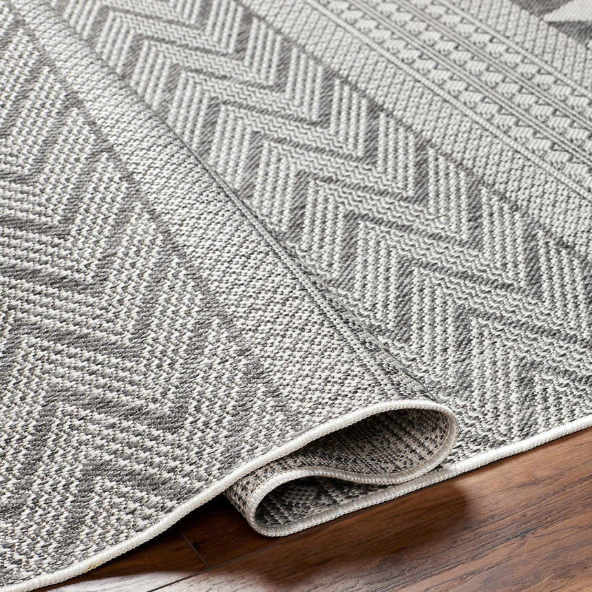 Close-up of the Asif Gray Area Rug showing its charcoal, light gray, and off-white farmhouse-style chevron pattern. Fold