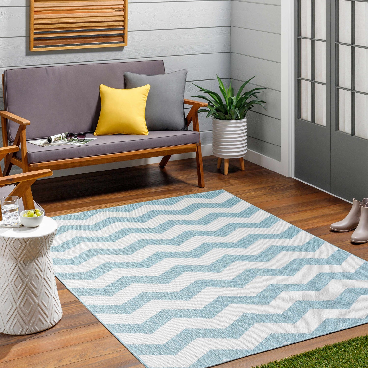 Patio scene with a light blue chevron Cheri Thatch Area Carpet, gray loveseat, and white accent table. Roomscene-Rectangle