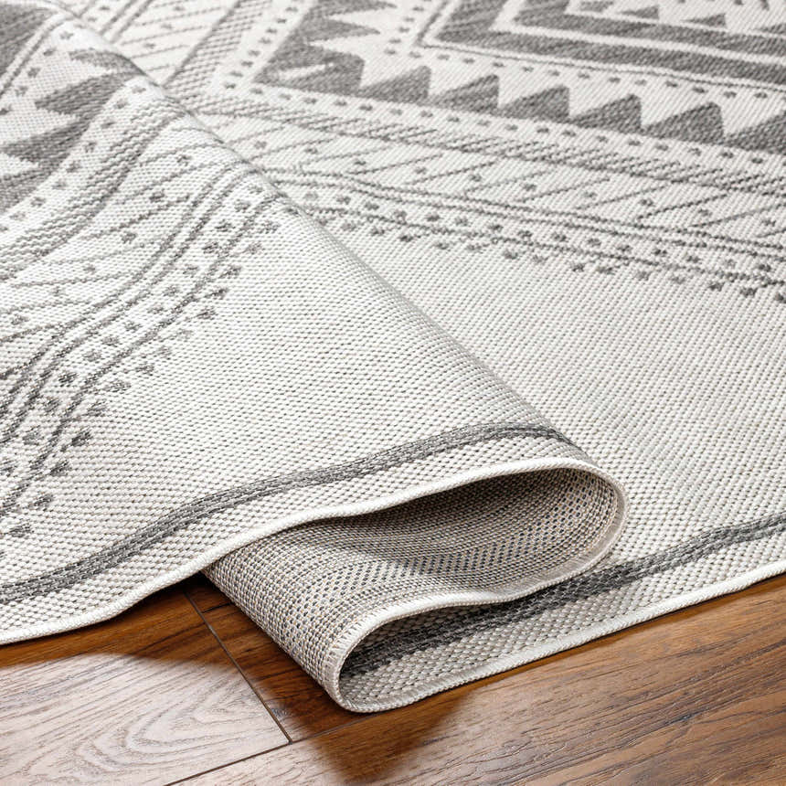 Close-up of the Deana Light Gray Area Rug showing its bohemian pattern, woven texture, and gray and off white colors. Fold