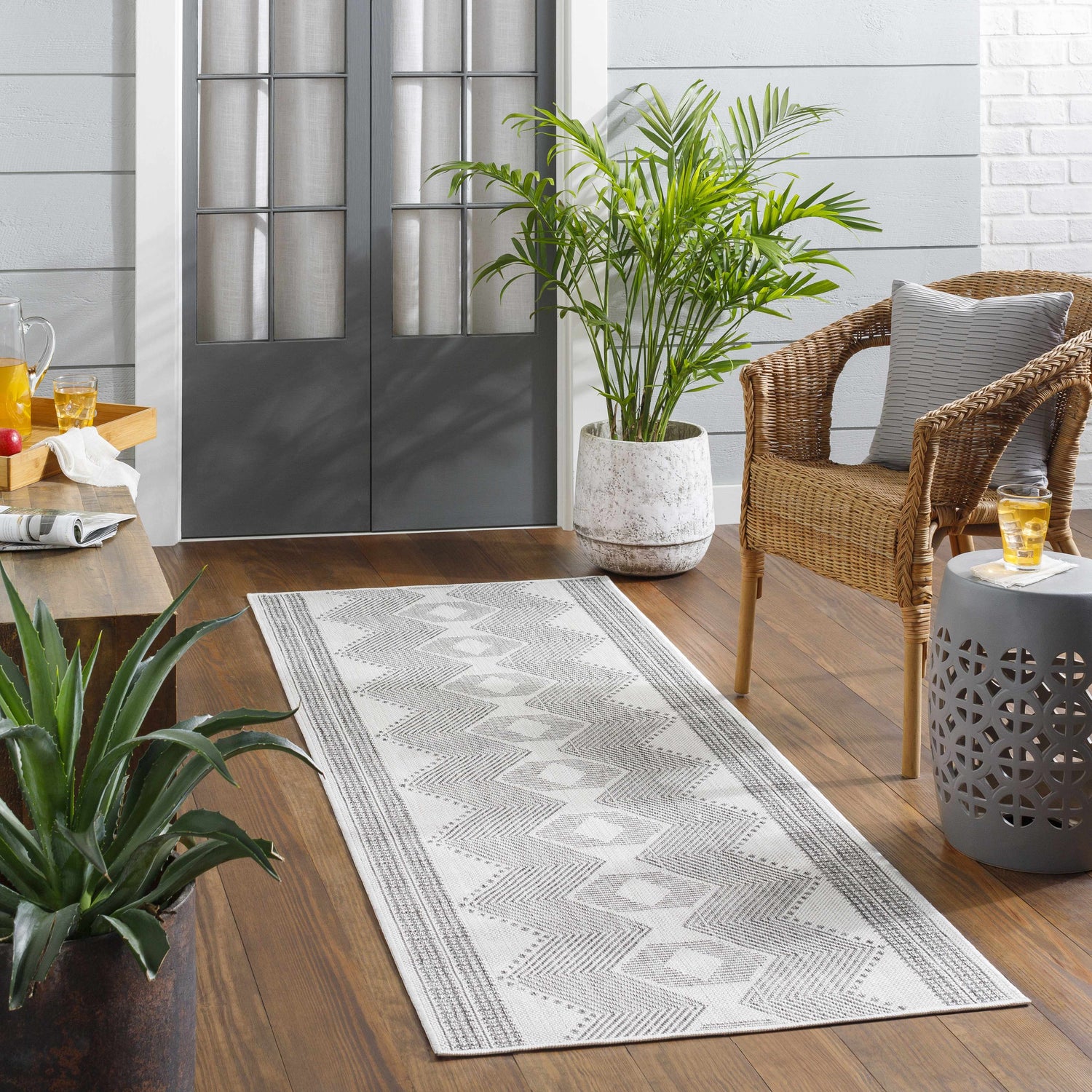 Outdoor patio scene with Evana Gray Area Rug, wicker chair, potted plants, and gray accent table. Roomscene-Runner