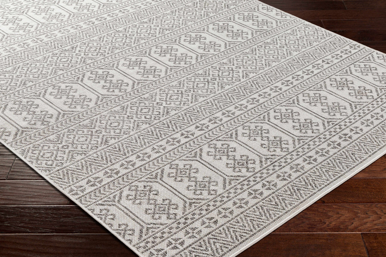 Close-up of the Kalb Area Carpet showing its light gray, off-white, and charcoal bohemian pattern and machine-woven texture. Corner