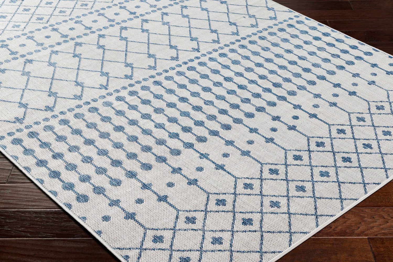Close-up of Lali Blue & Gray Area Rug showing geometric trellis pattern in denim blue on a light gray background. Corner
