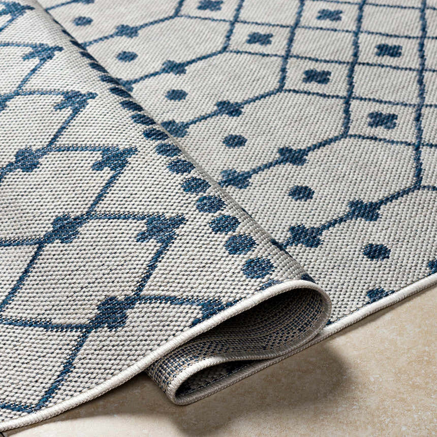 Close-up of Lali Blue & Gray Area Rug showing geometric trellis pattern and woven texture on a tan tile floor. Fold