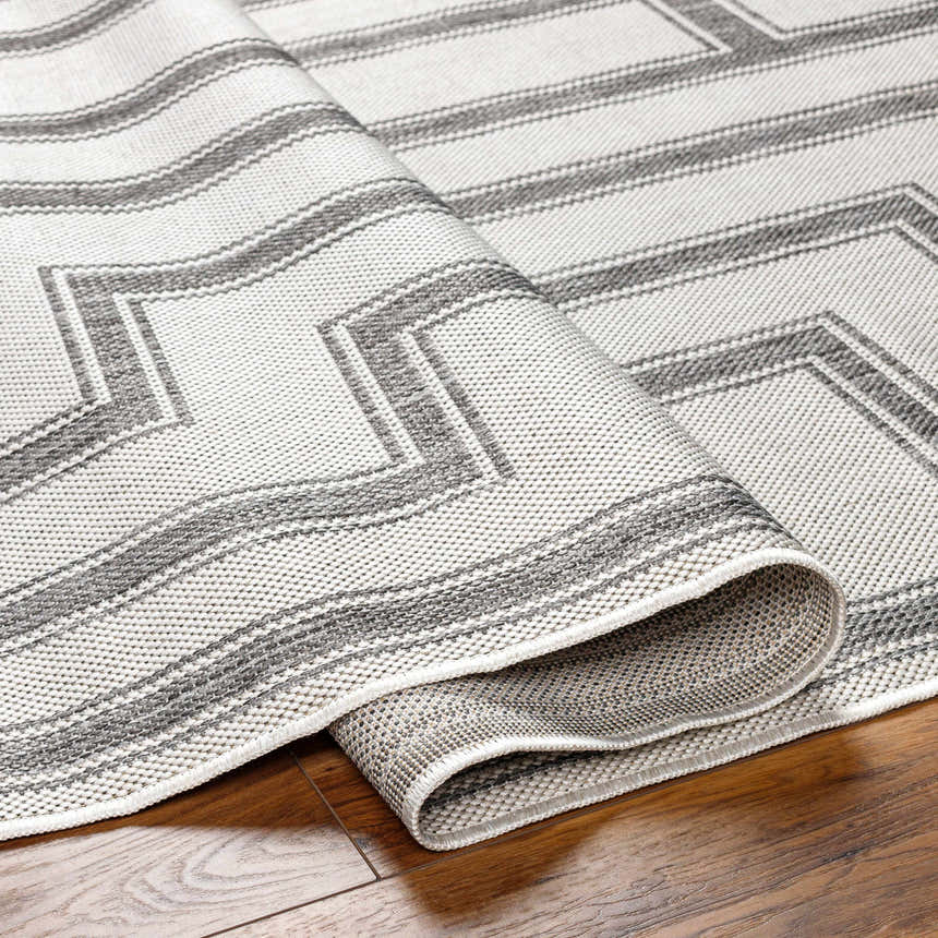 Close-up of the Taro Light Gray Area Rug featuring a geometric pattern and woven texture on a wood floor. Fold