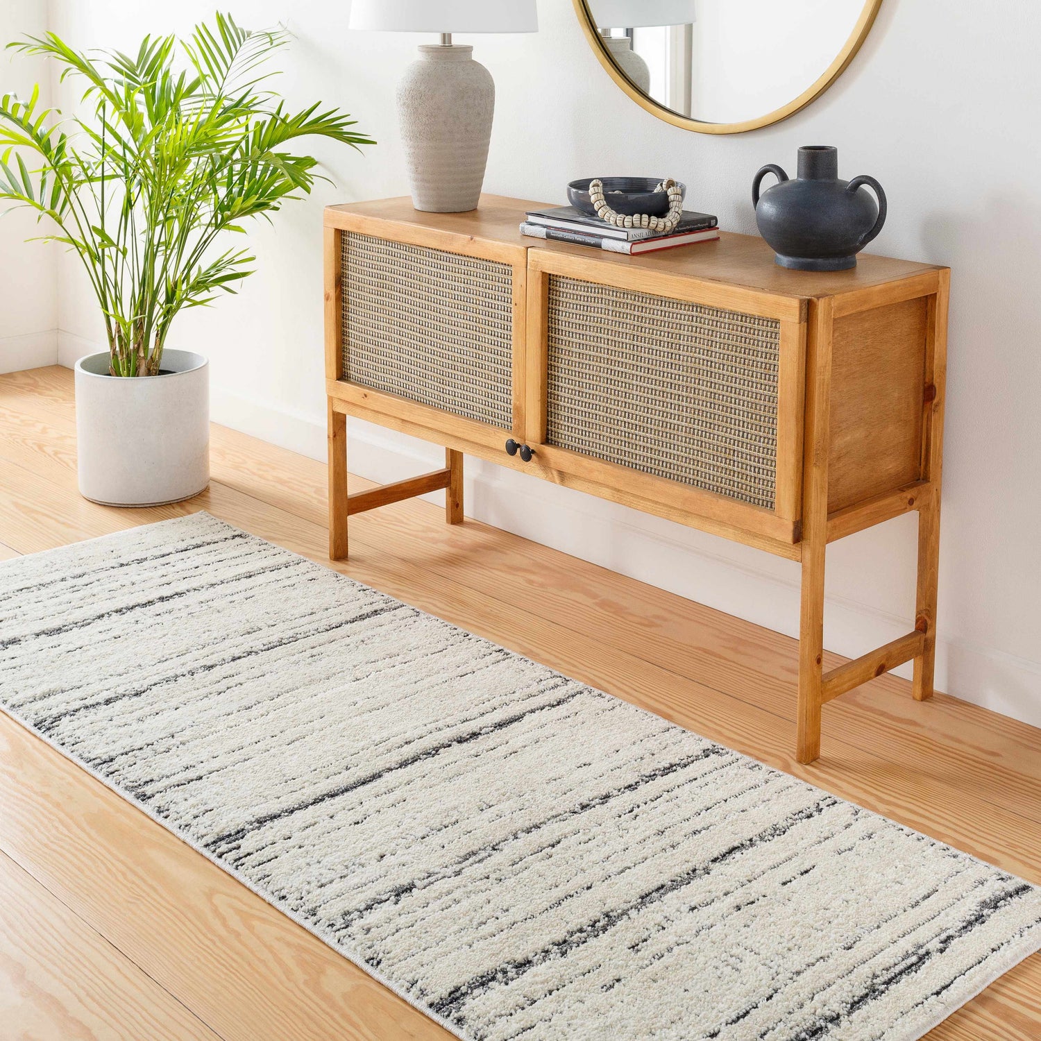 Entryway with Enli Area Rug runner in charcoal and ivory, wood console table, plant, and round mirror. Roomscene-Runner