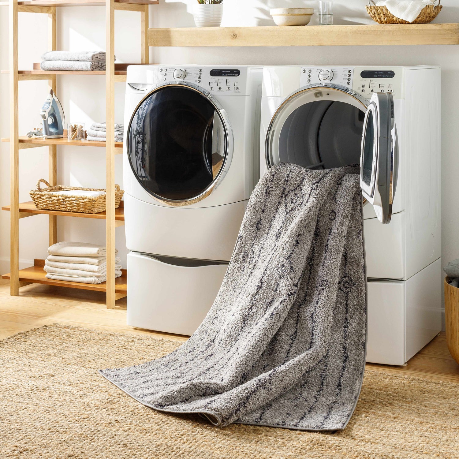 Laundry room scene with a Demi Gray Washable Area Rug partially inside a front load washing machine. Washing-Machine