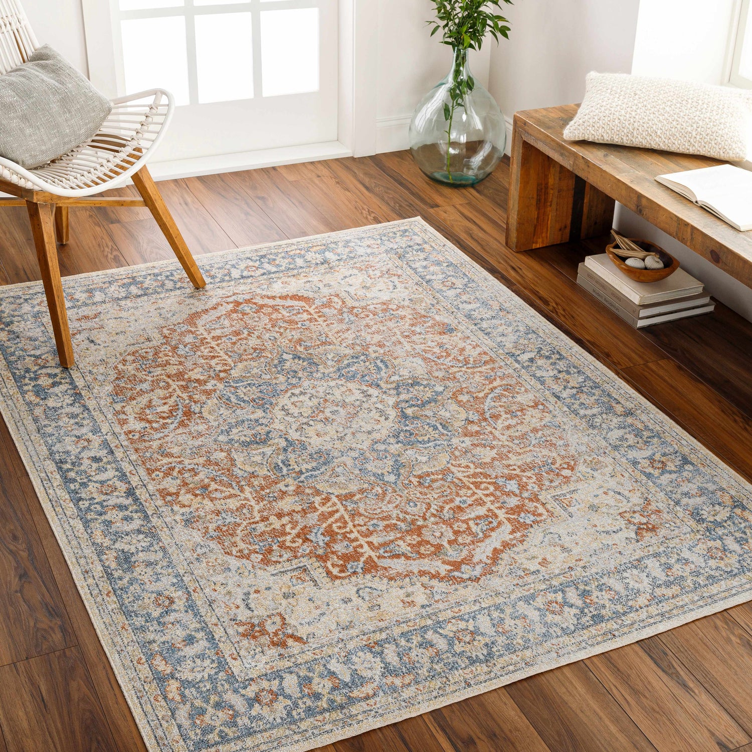 Living room scene with Emke Rust Washable Area Rug in dark beige, gray, and nutmeg colors, styled with a white chair and wood bench. Roomscene-Rectangle