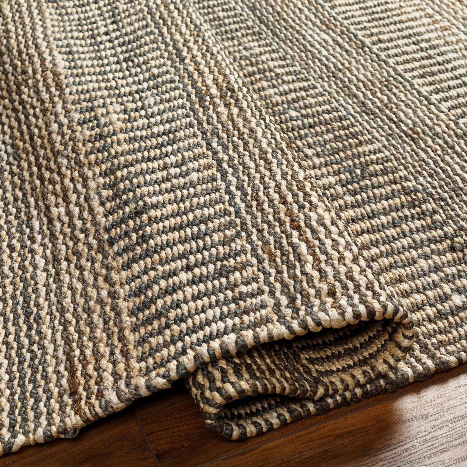 Close-up of the Gray Elle Area Rug showing its hand-woven jute texture and geometric pattern in black, tan, and off-white. Fold