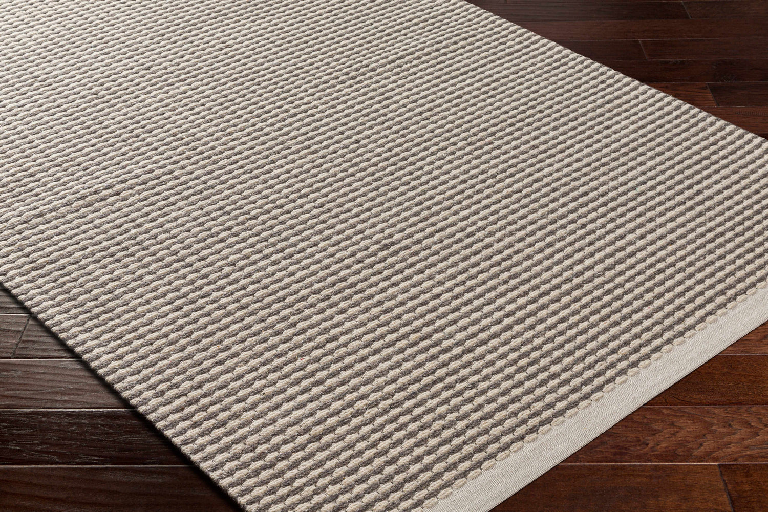Close up of textured Black Emlen Area Rug on dark wood floor. Hand woven wool rug in cream and gray. Corner