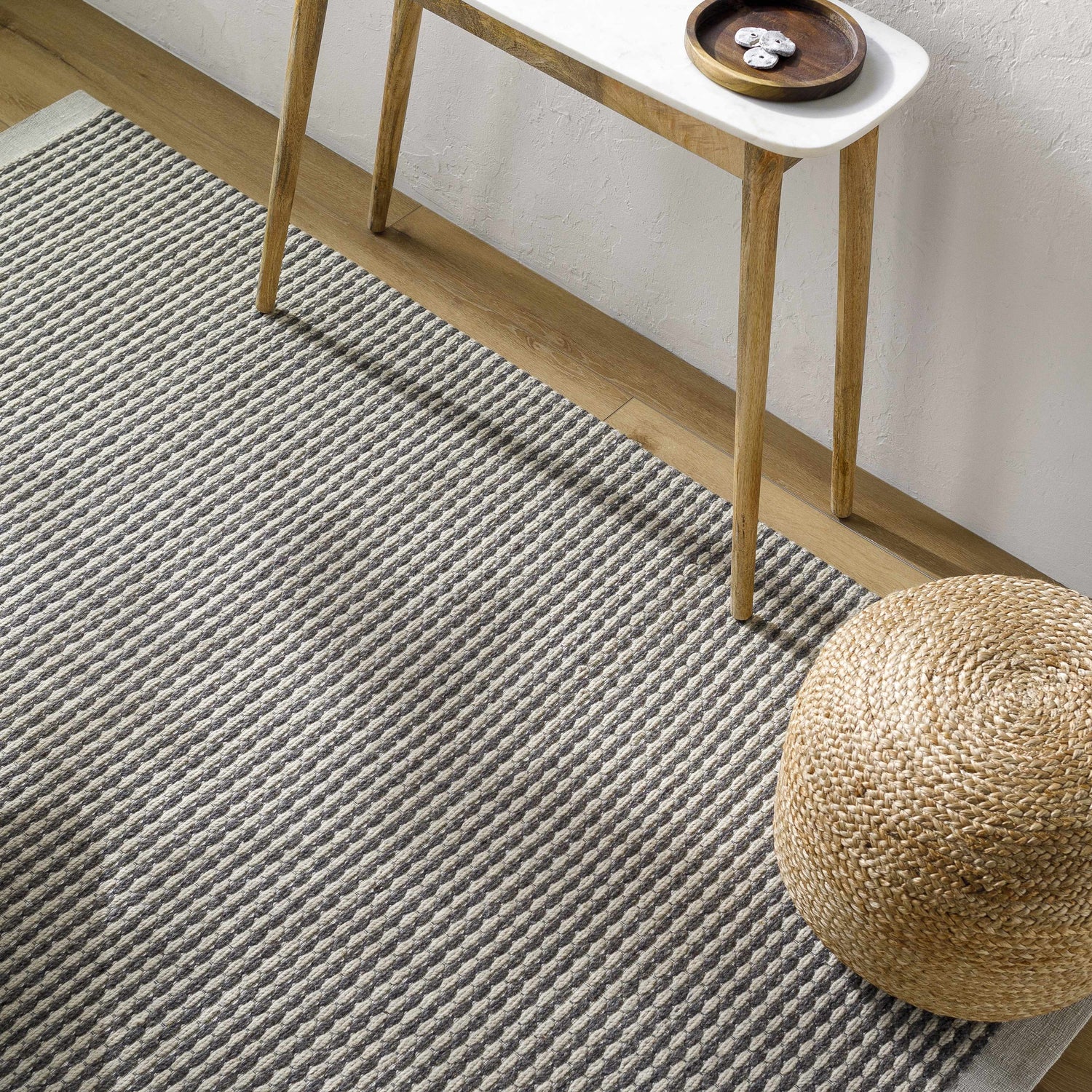 Close-up of the Black Emlen Area Rug showing its woven texture and gray and cream stripes, styled with a side table and pouf. Styleshot