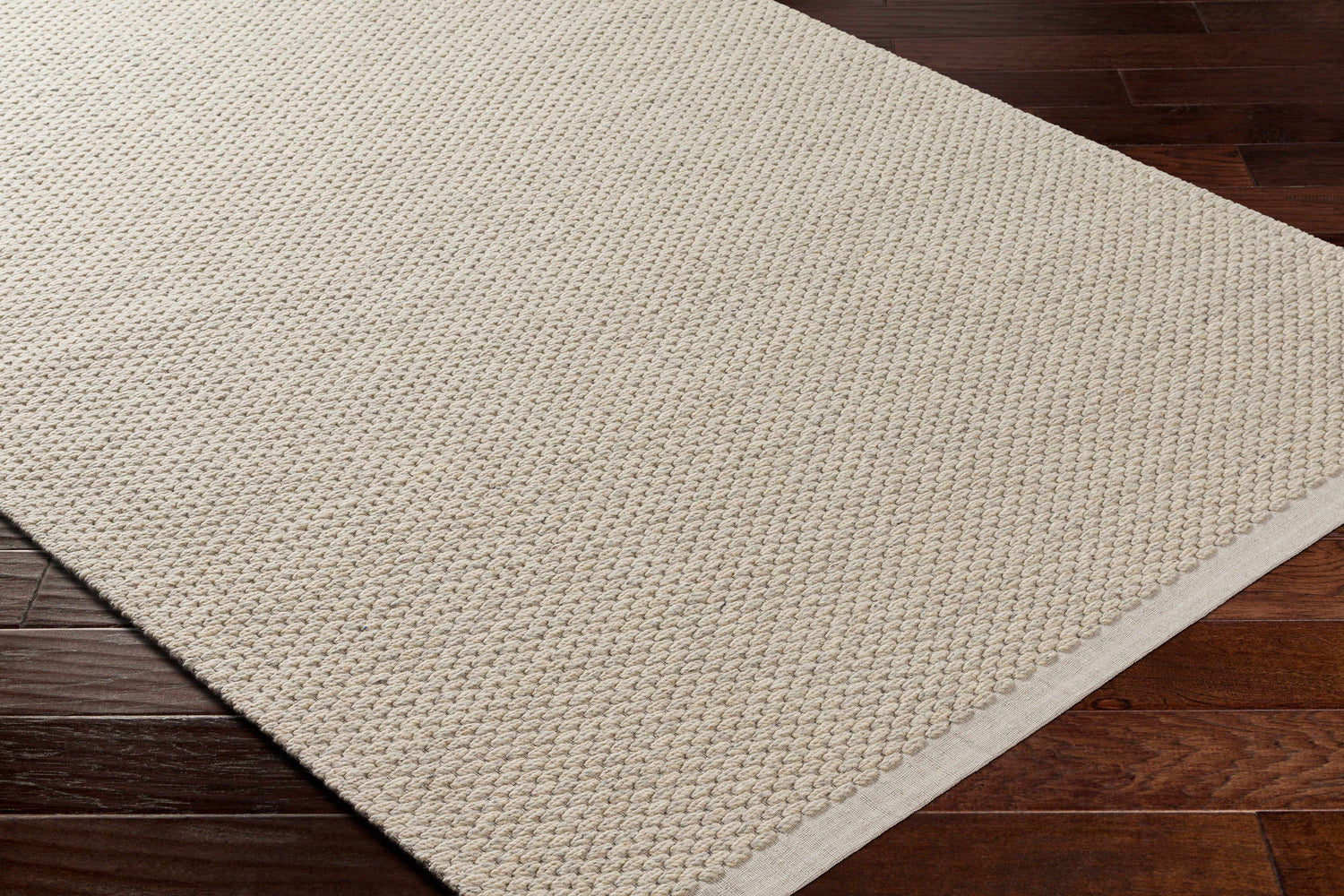 Close-up of the Beige Emlen Area Rug showing its hand woven texture and neutral bone color on dark wood flooring. Corner