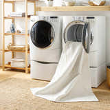 Laundry room scene with Amani White Washable Rug partially in the washing machine, layered over a jute rug. Washing-Machine