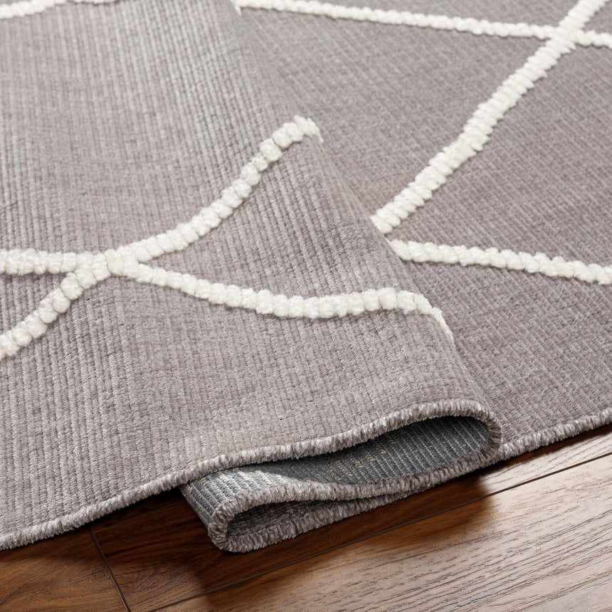Close-up of Amani Gray Washable Rug showing geometric white pattern and soft gray texture on a wood floor. Clearance rug. Fold