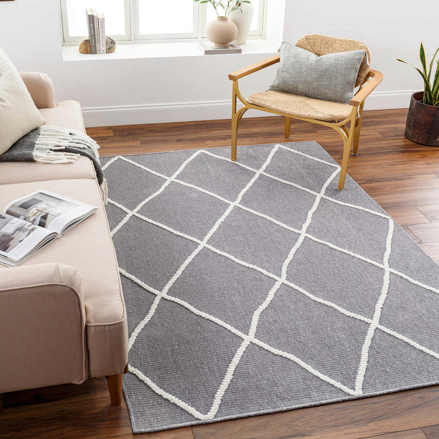 Living room scene with a gray Amani Washable Rug featuring a white geometric pattern, styled with a beige sofa and woven chair. Roomscene-Rectangle
