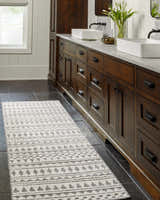 Bathroom scene with a Cloud Gray Cili Washable Area Rug runner in front of dark wood cabinets and black tile floor. Roomscene-Runner