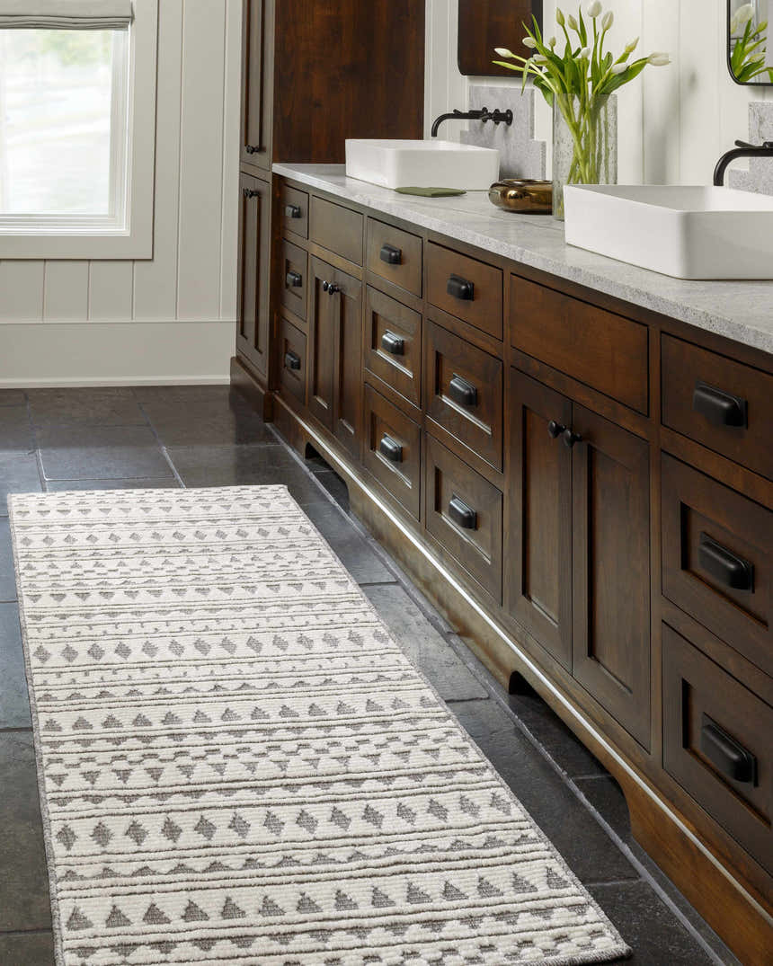 Bathroom scene with a Cloud Gray Cili Washable Area Rug runner in front of dark wood cabinets and black tile floor. Roomscene-Runner