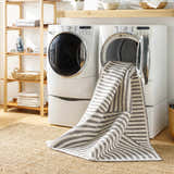 Laundry room scene with Deron Gray Rainbow Washable Rug coming out of the dryer, layered on a jute rug. Washing-Machine