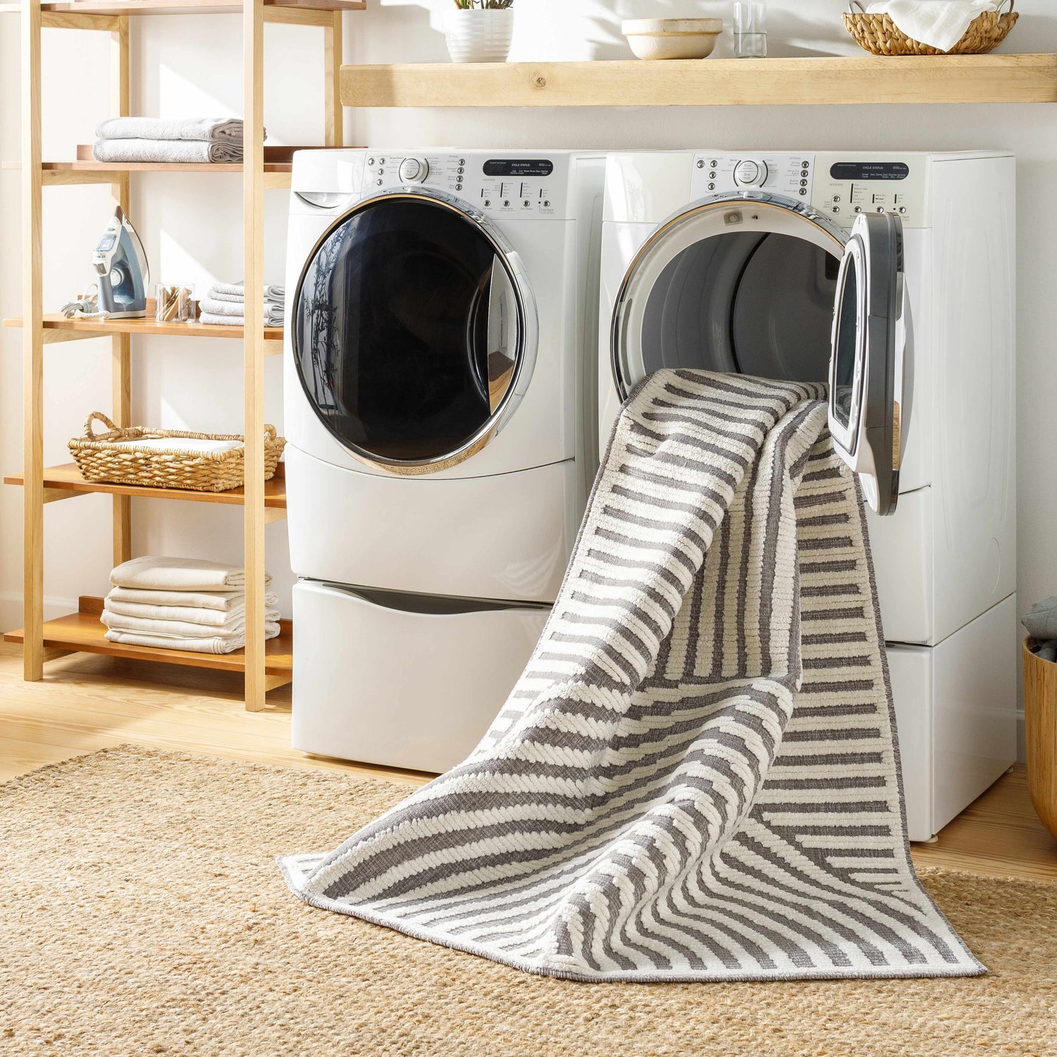 Laundry room scene with Deron Gray Rainbow Washable Rug coming out of the dryer, layered on a jute rug. Washing-Machine