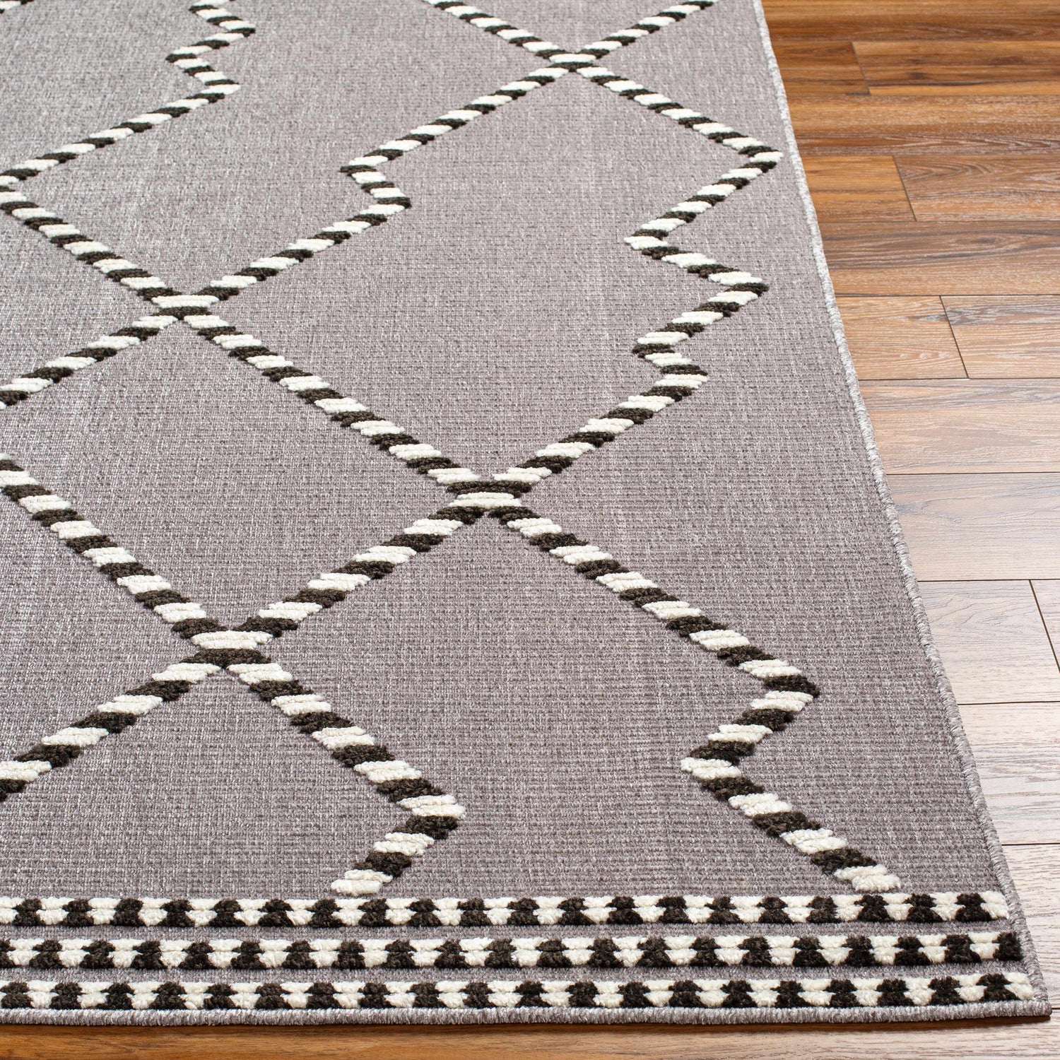Close-up of the Rolf Textured Washable Rug in bone, onyx black, and taupe with a geometric diamond pattern. Front