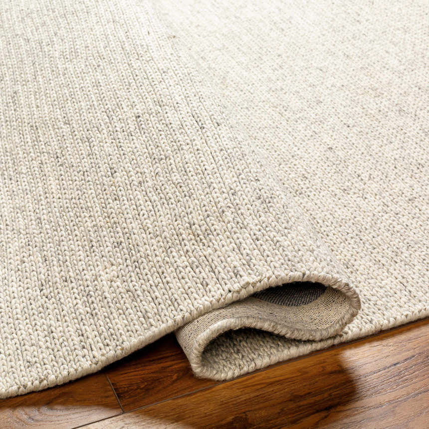 Close-up of the hand woven Alyra Beige Solid Area Rug showing texture and color on a wood floor. Fold