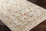 Close-up of the Asabi Tan Textured Rug on a dark wood floor. Features brick red, navy, sage, and mustard floral patterns. Corner