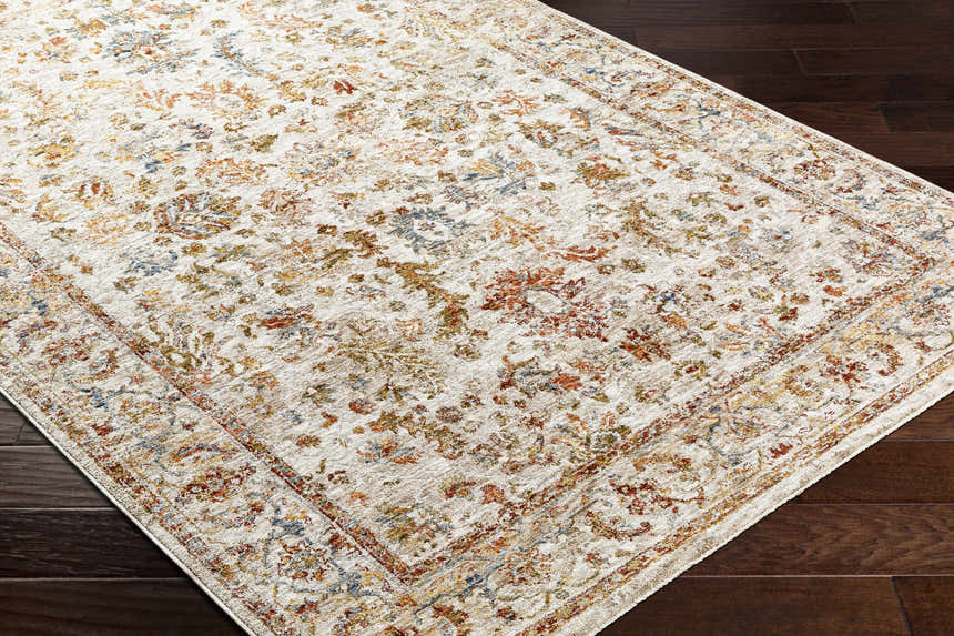 Close-up of the Asabi Tan Textured Rug on a dark wood floor. Features brick red, navy, sage, and mustard floral patterns. Corner