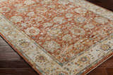 Close-up of the Duong Rust Textured Rug. Features a traditional floral pattern in brick red, sage, tan, and blue on a dark wood floor. Corner