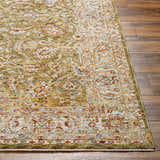 Close-up of the textured Dyan Green Rug on wood floor. Features brick red, mustard, and sage floral patterns. Front